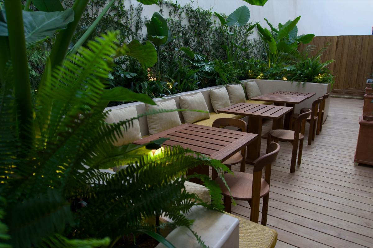 The terrace at the back: wooden tables and cushioned benches among the plants